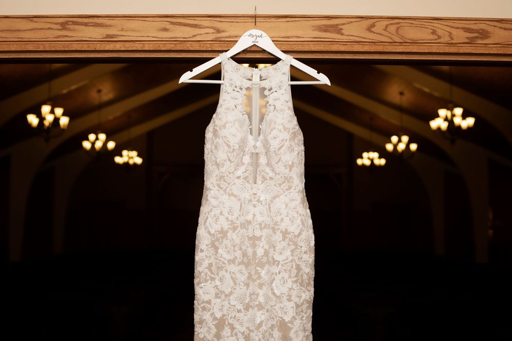 Detailed lace wedding dress hangs against wooden backdrop with soft lighting.
