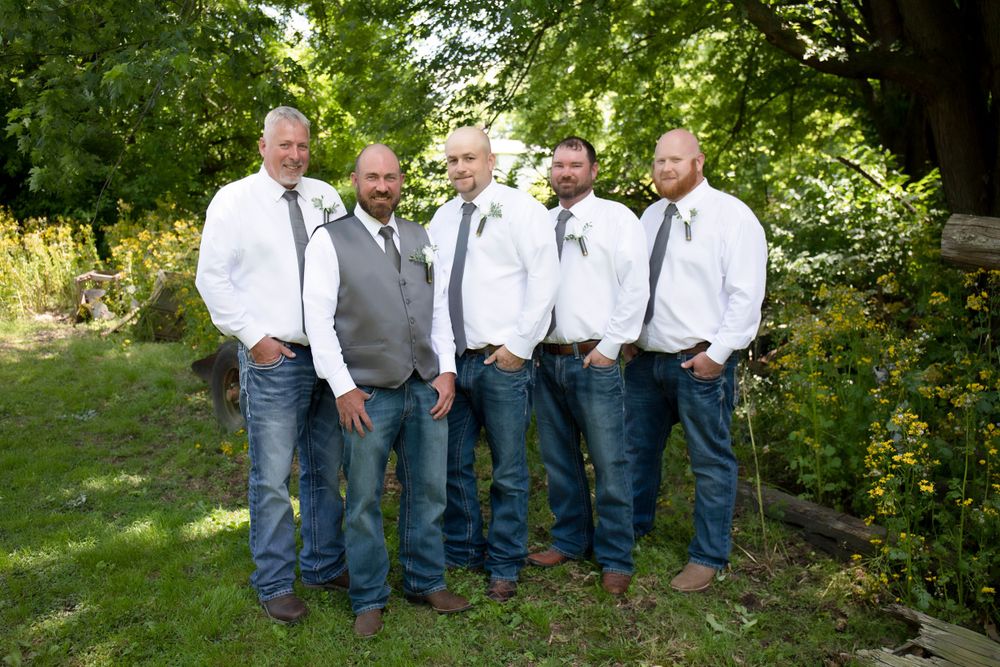 Groomsmen in white shirts and grey vests pose together in casual outdoor setting.