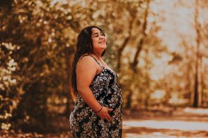 A woman in a floral dress poses confidently during an outdoor maternity photoshoot.