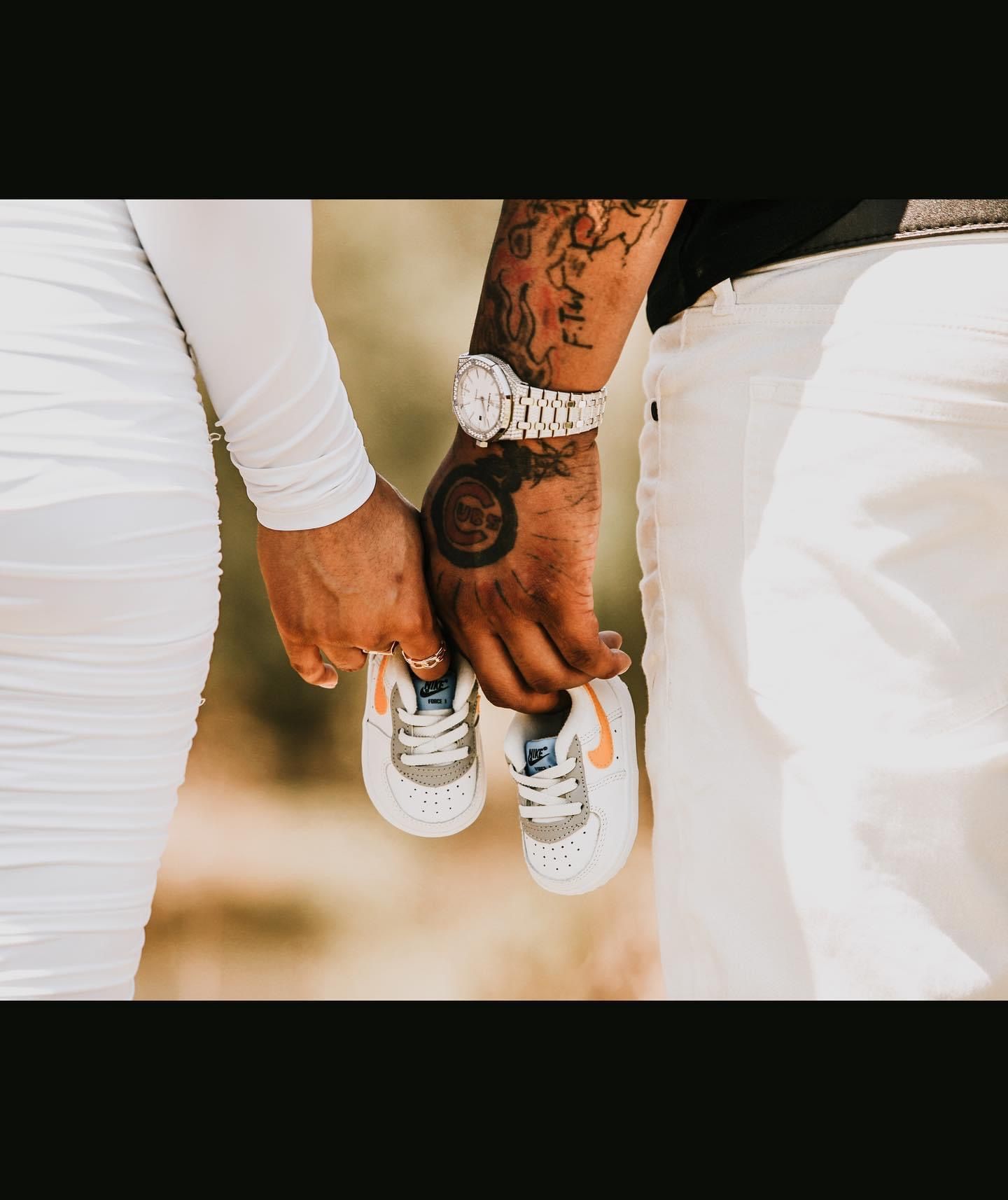 Close-up of hands holding baby shoes with visible tattoo artwork.