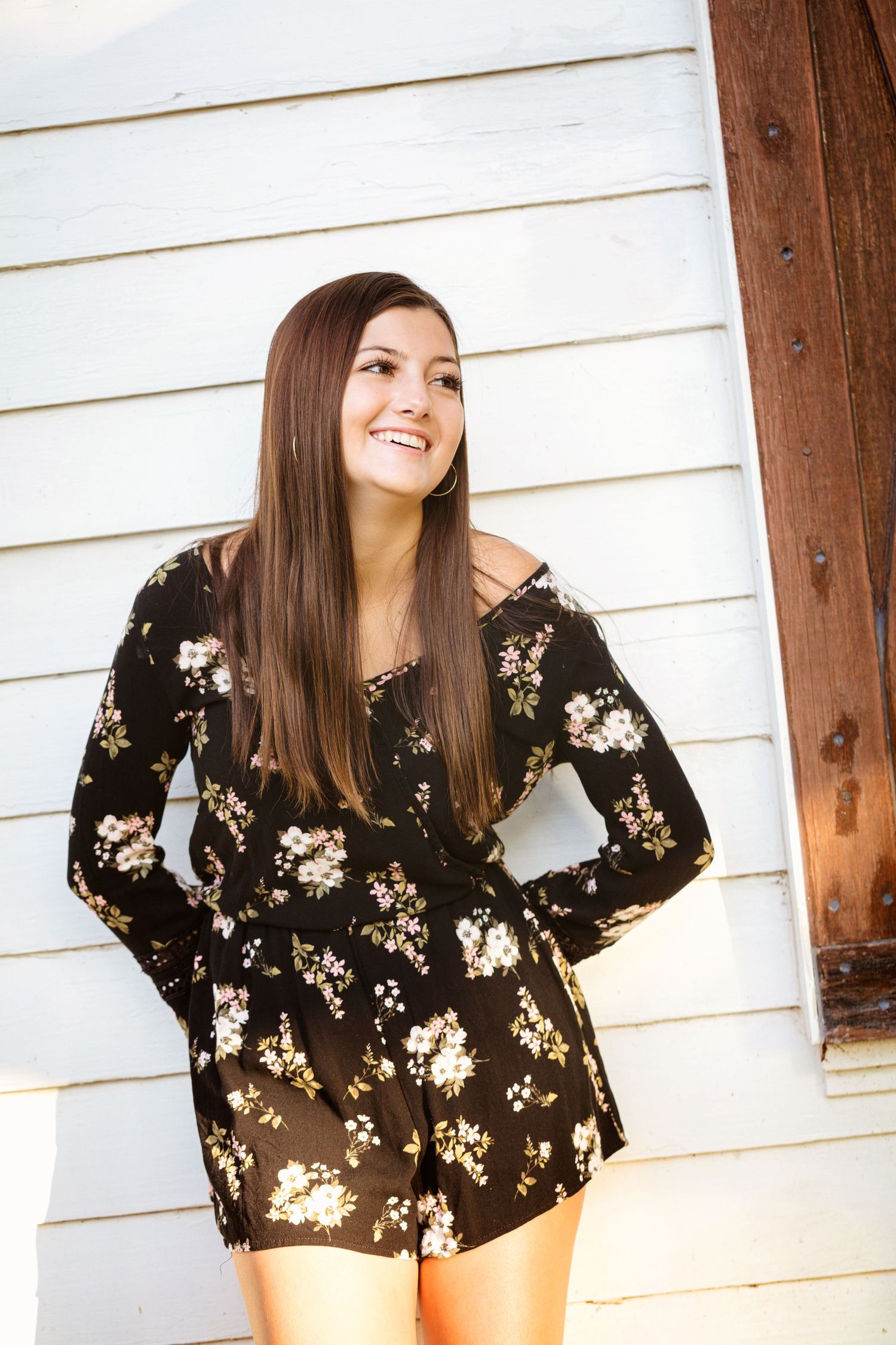 Fashion portraits against white siding wearing black floral top in natural lighting.