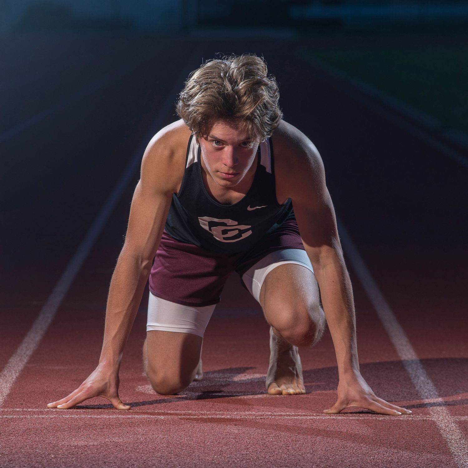 Runner in starting position on red track during dramatic low-angle photo shoot.
