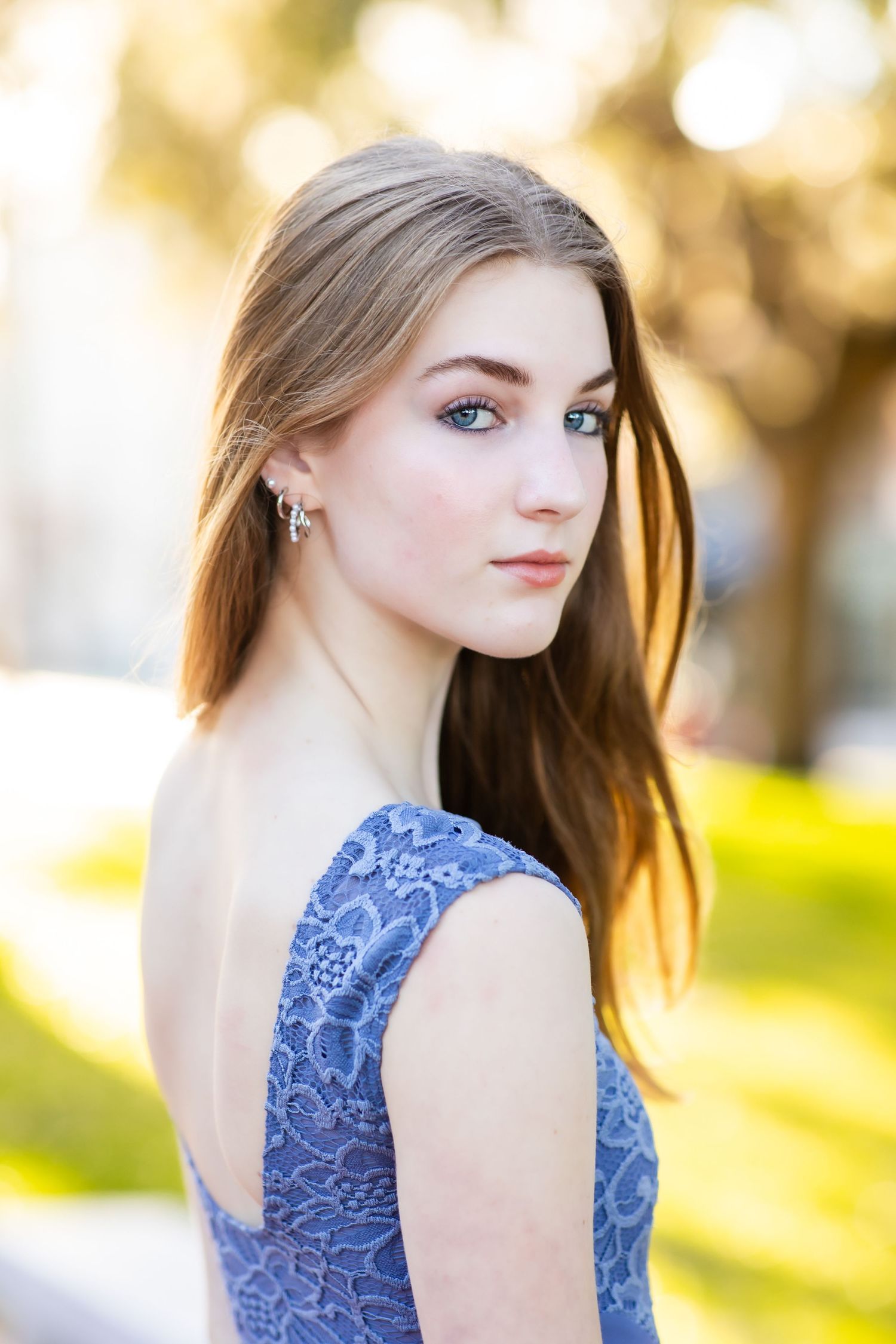 Elegant outdoor portrait in a blue lace dress with natural lighting and bokeh effect.