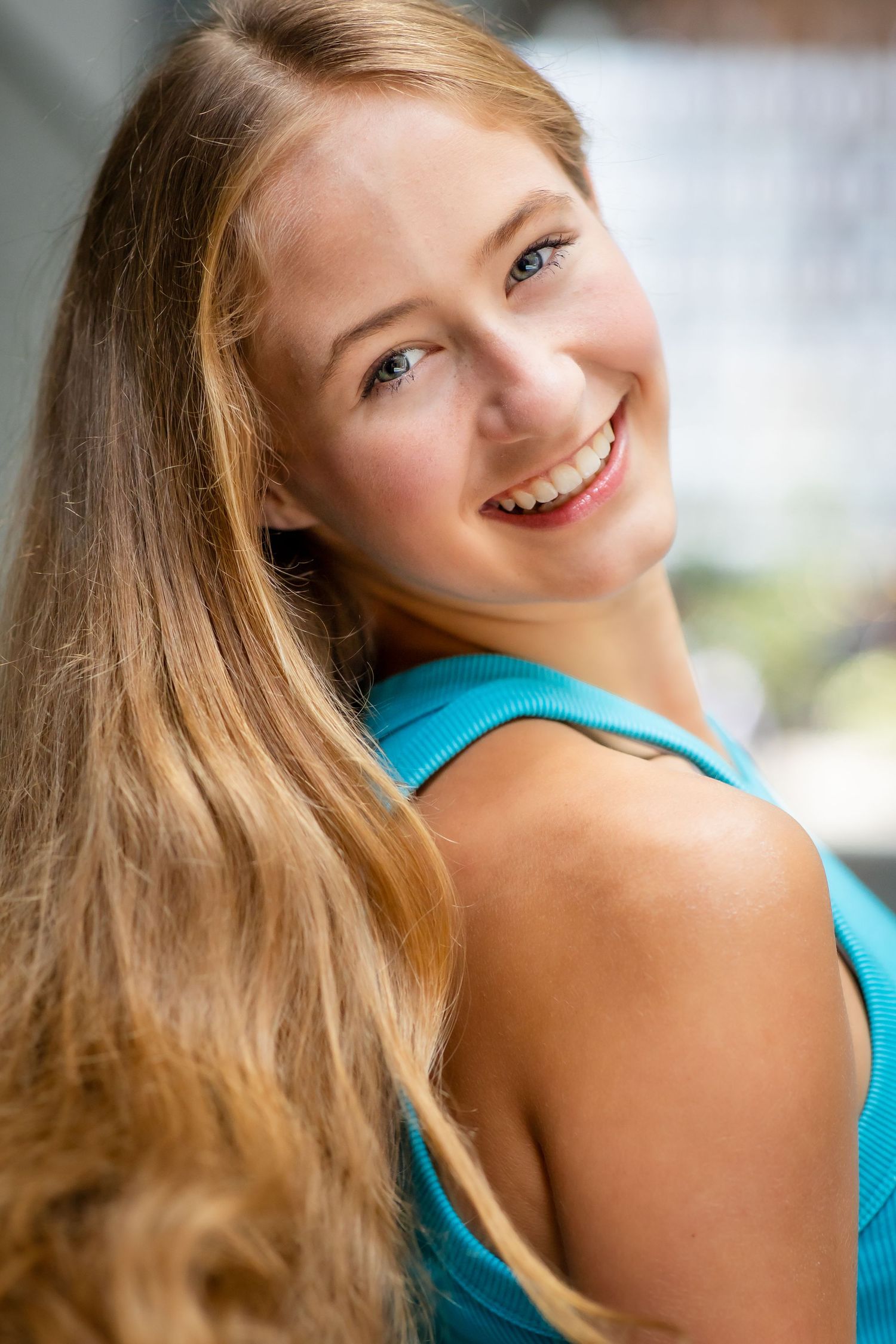 Portrait of someone with long blonde hair smiling while wearing a turquoise top.