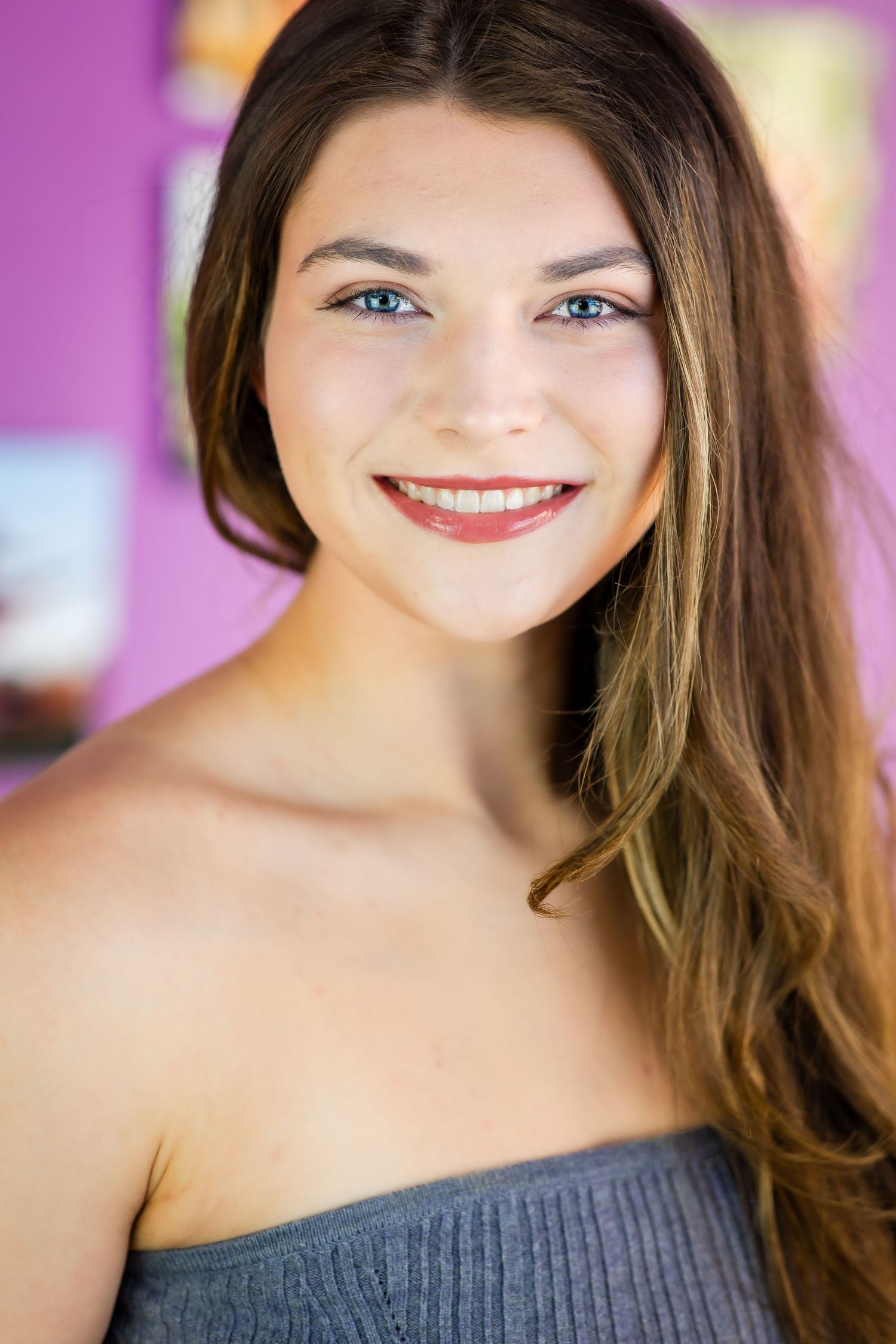 Professional headshot of a young performer with brown hair against a purple background.
