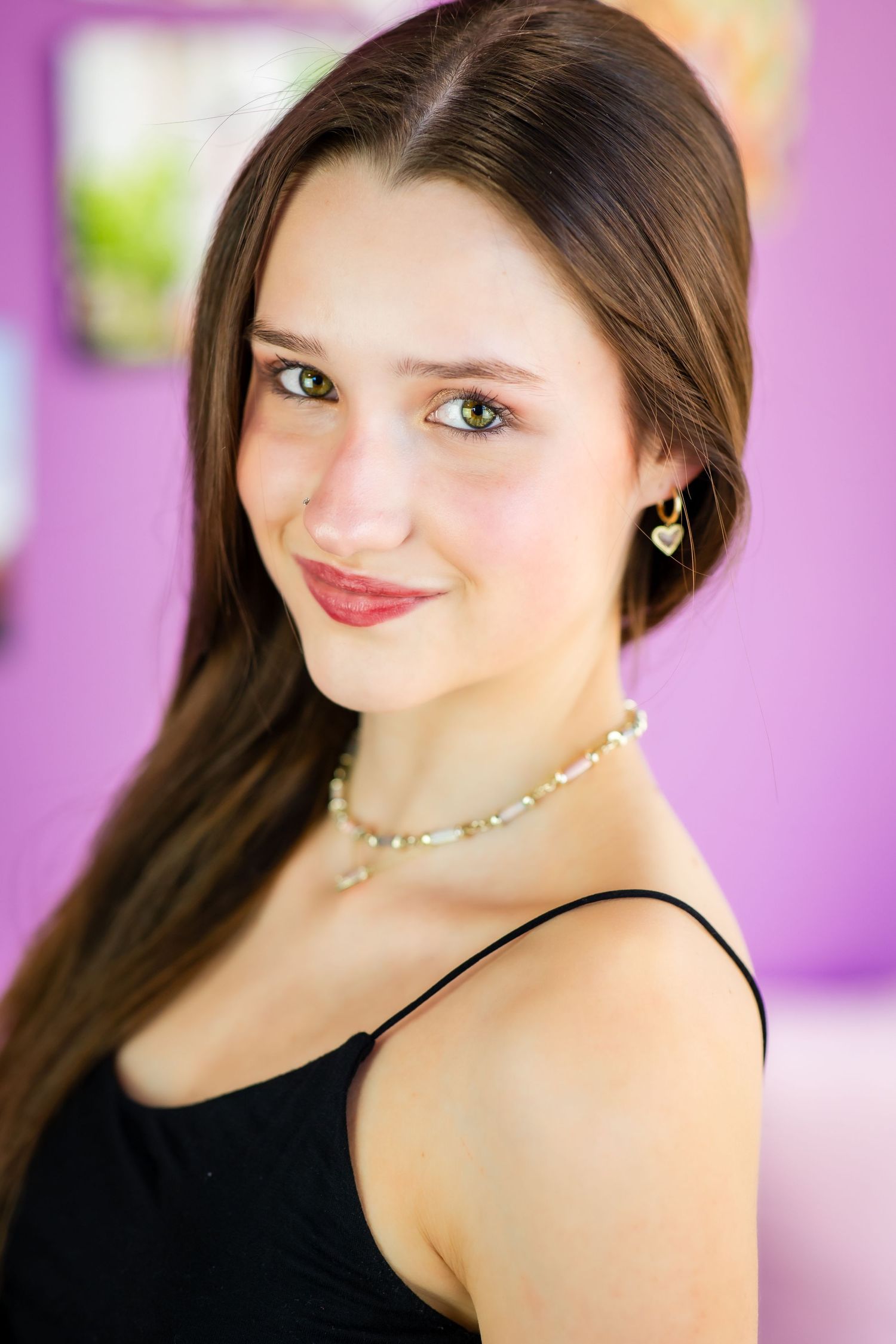 Portrait of a performer in black top and delicate necklace against purple backdrop.