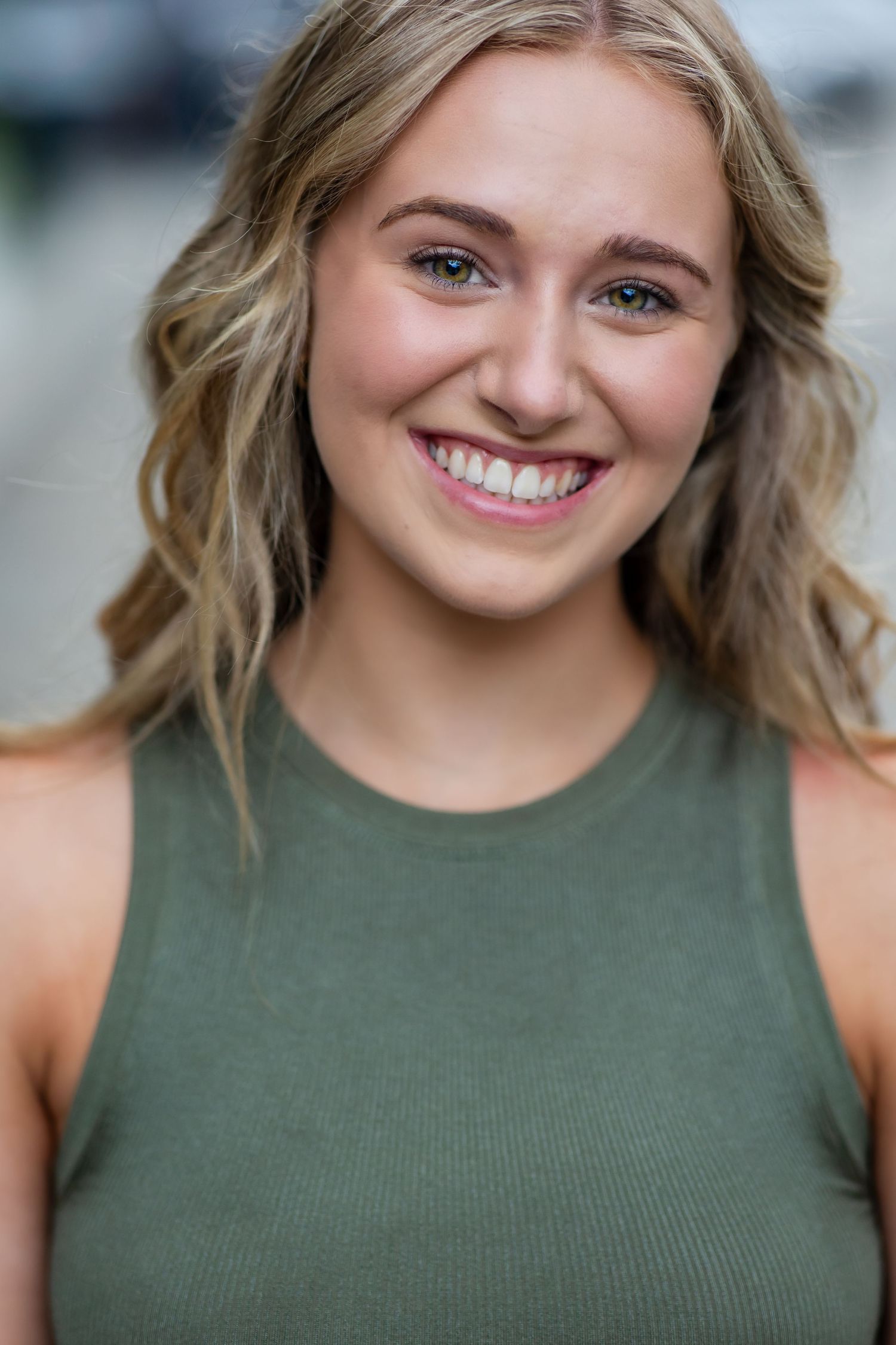 Portrait of someone in olive green tank top with natural makeup and wavy blonde hair.