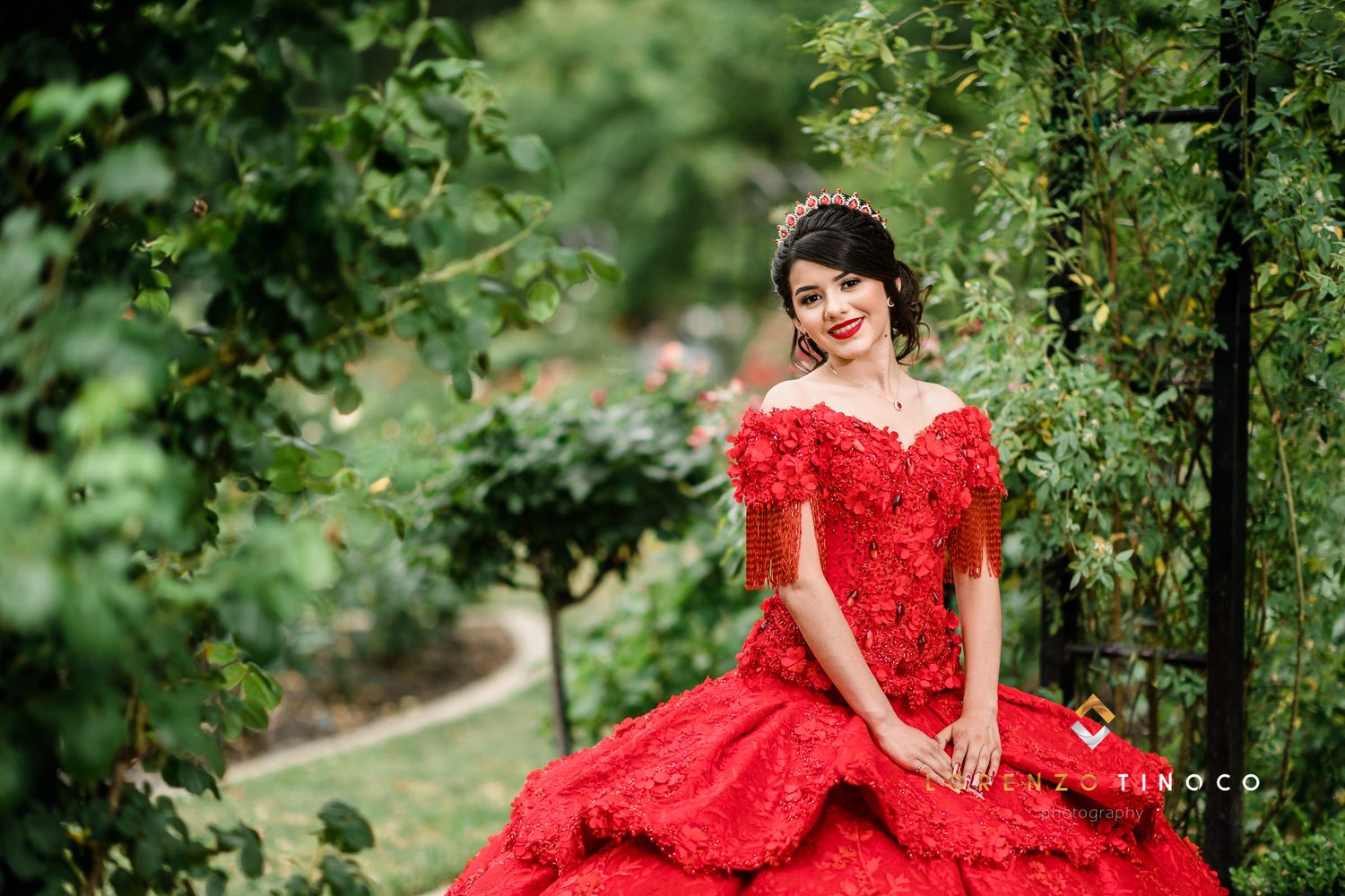 Red ballgown dress contrasts beautifully with lush garden greenery in outdoor portrait.