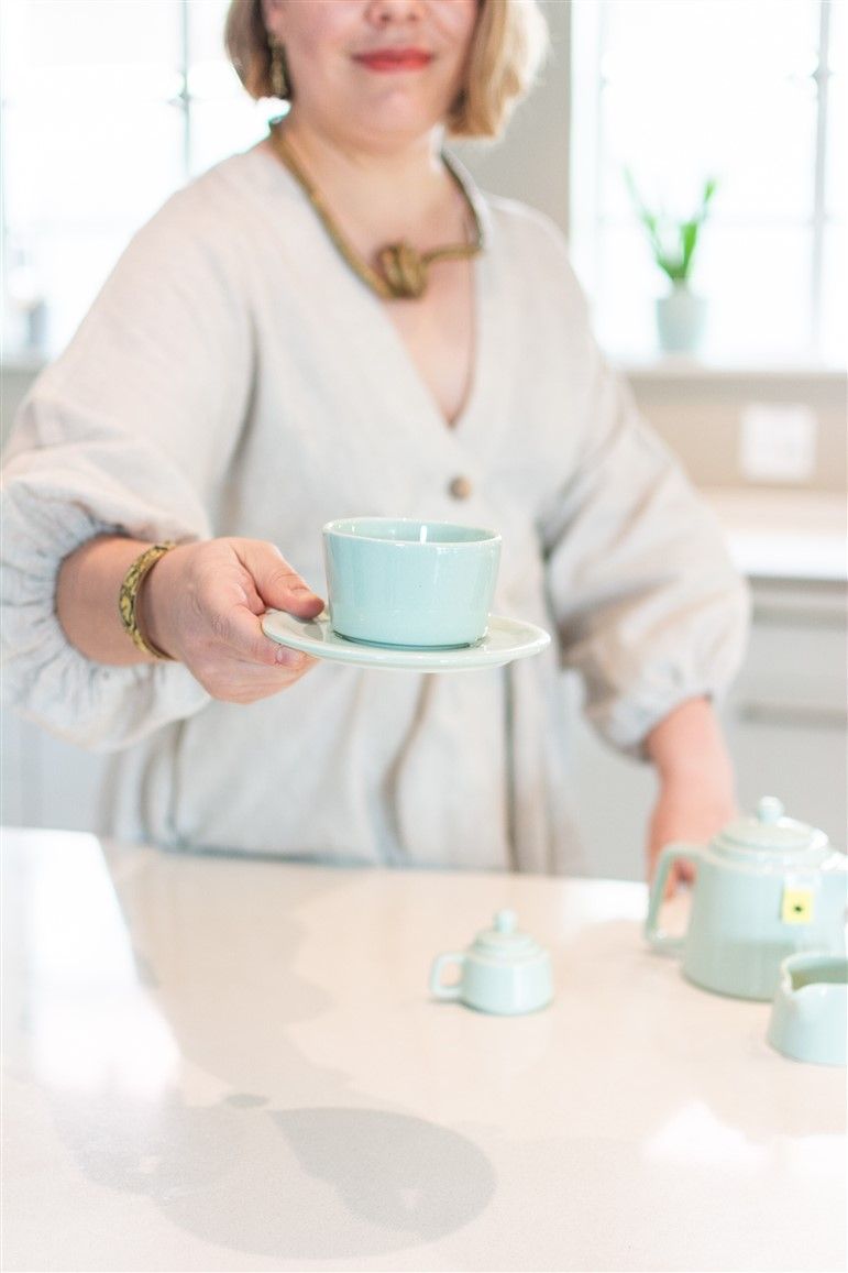 Hand holding mint green teacup over white table with matching tea set.