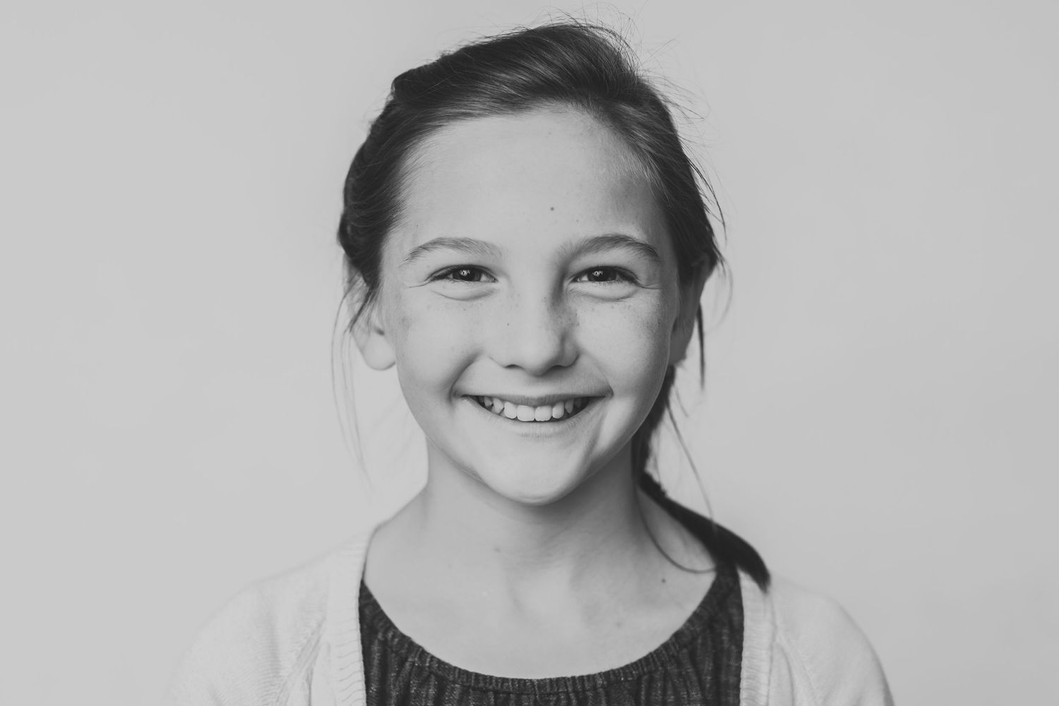 Black and white portrait of a young child with a wide, joyful smile and hair pulled back.