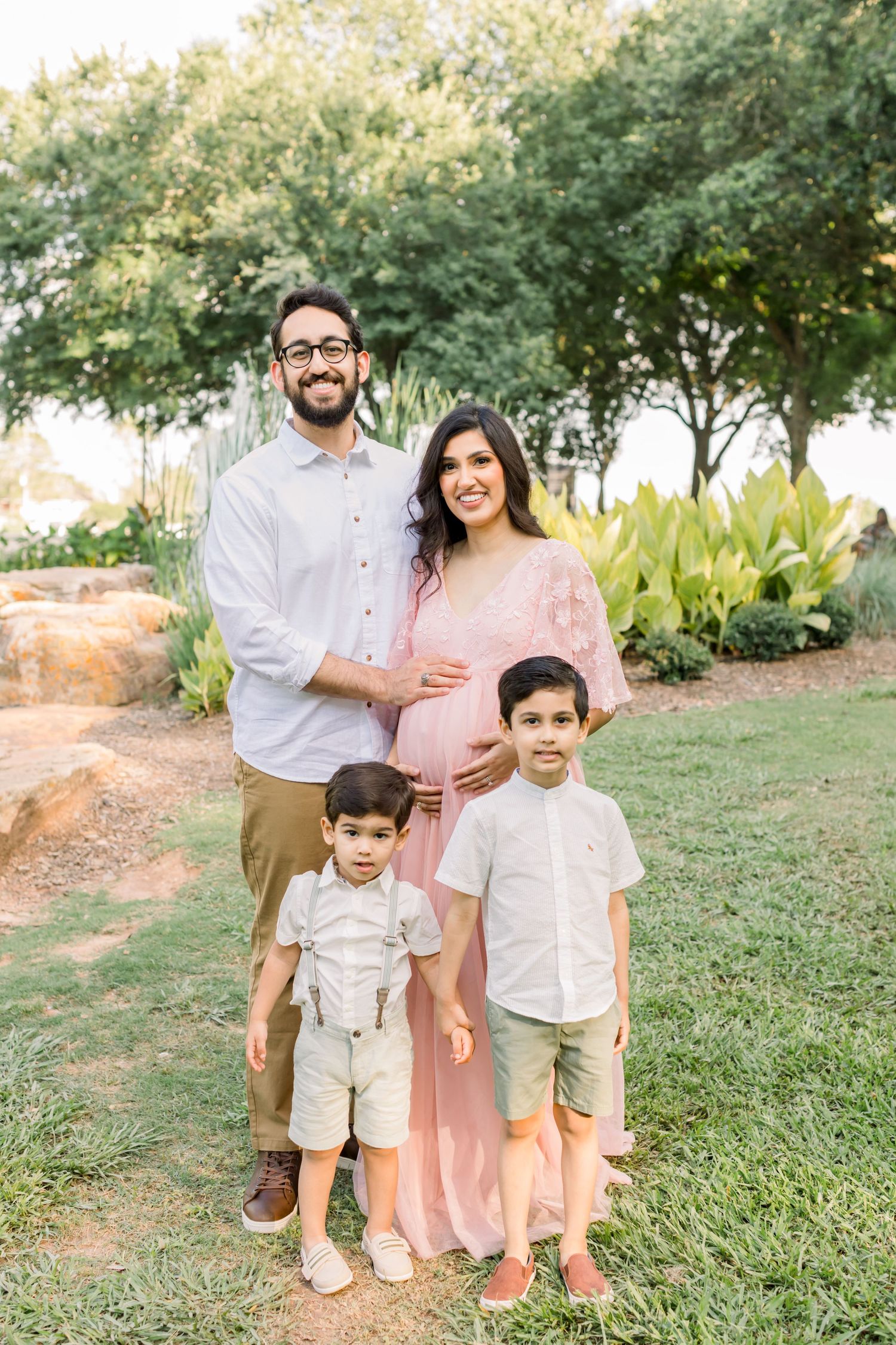 A family of four poses together outdoors with greenery, trees and rocks in the background.