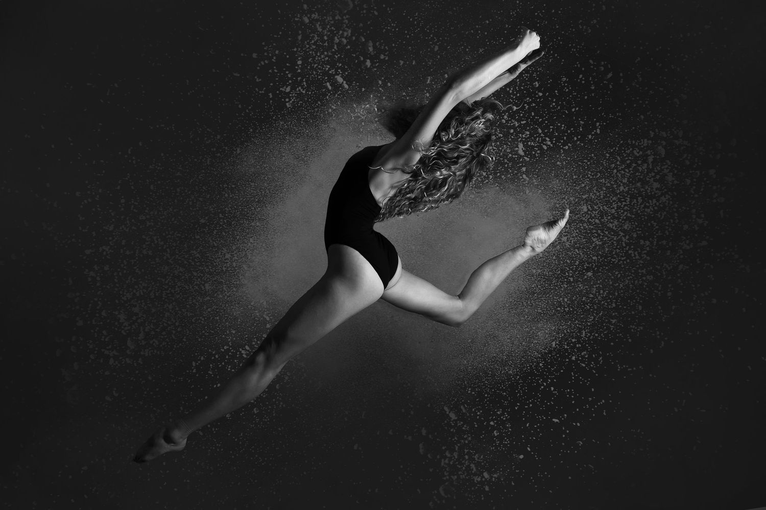 black and white photo of female dancer in black leotard jumping with flour effect