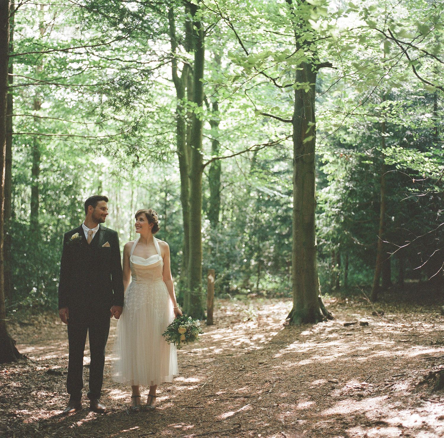 Bride and groom walking together in a sunlit forest setting.