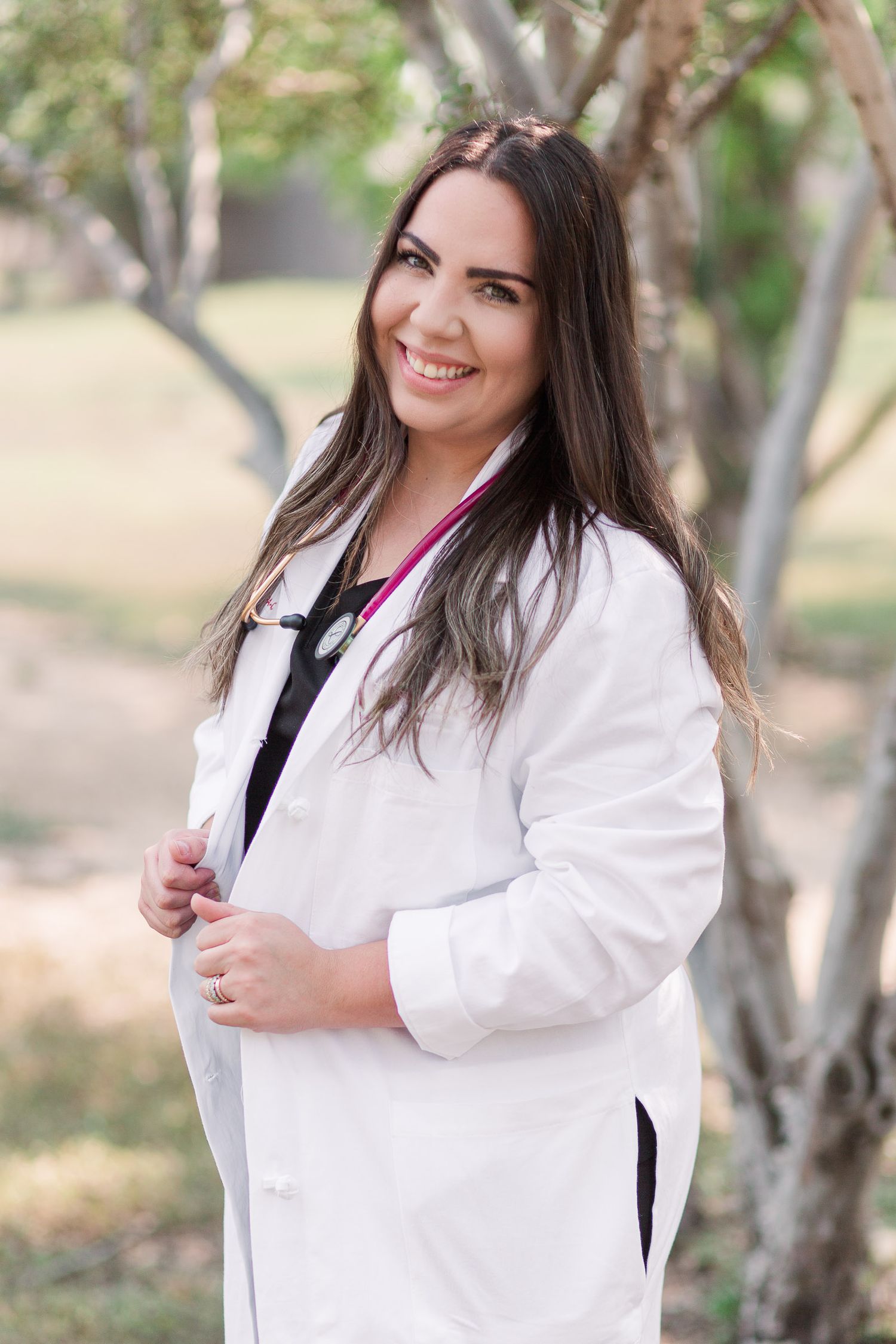 Professional headshots outdoors of person in white coat against natural backdrop.