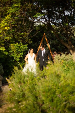 bride and groom holding hands walking away from their ceremony with greenery and arch in background