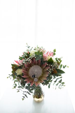 large floral bouquet with king proteas and deceased family pins attached in large vase