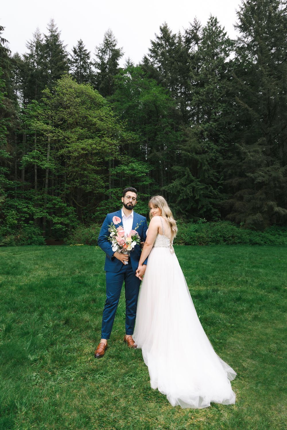 A newly wed couple poses for the camera in a wide shot portrait showing the forest.