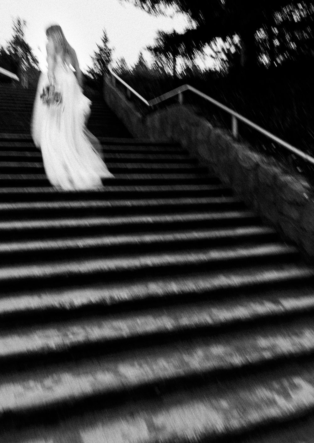 A bride runs up a set of stairs, holding her bouquet at her side. Her dress flows nicely and the motion is blurred artsy