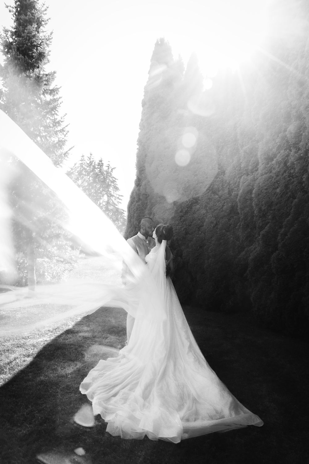 A wedding portrait of newlyweds kissing, the enormous veil flows in the wind.
