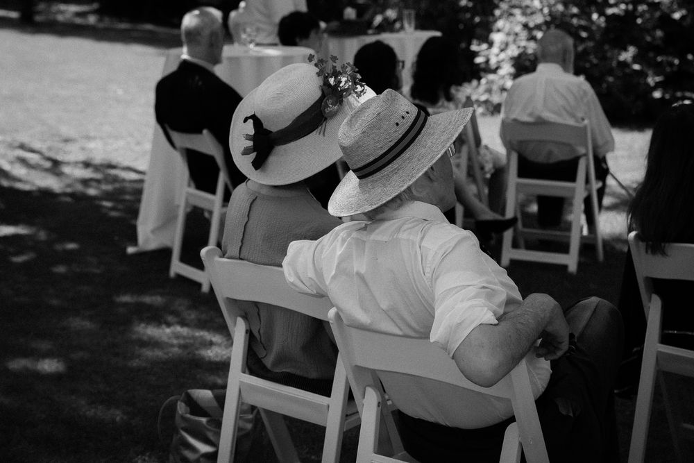 An older couple wears matching sun hats as they watch a jewish wedding ceremony in the heat