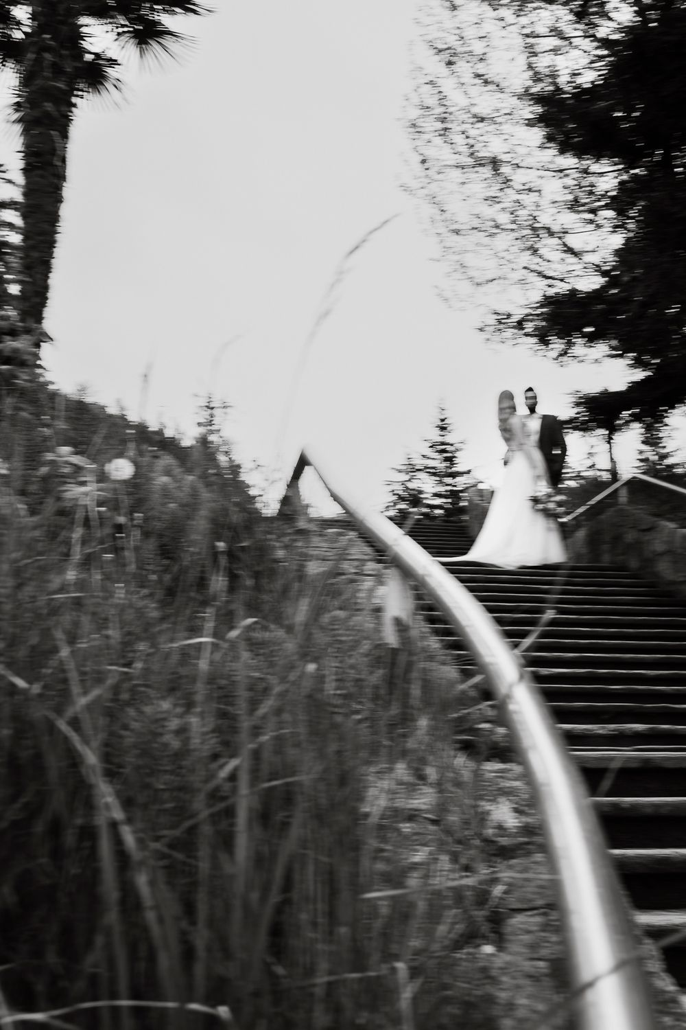 A bride and groom stand on a set of stairs for a photo wearing a white wedding dress and black tux. There is motion blur