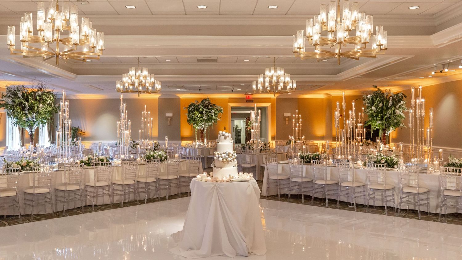 Luxurious ballroom set for wedding reception with crystal chandeliers and round tables.
