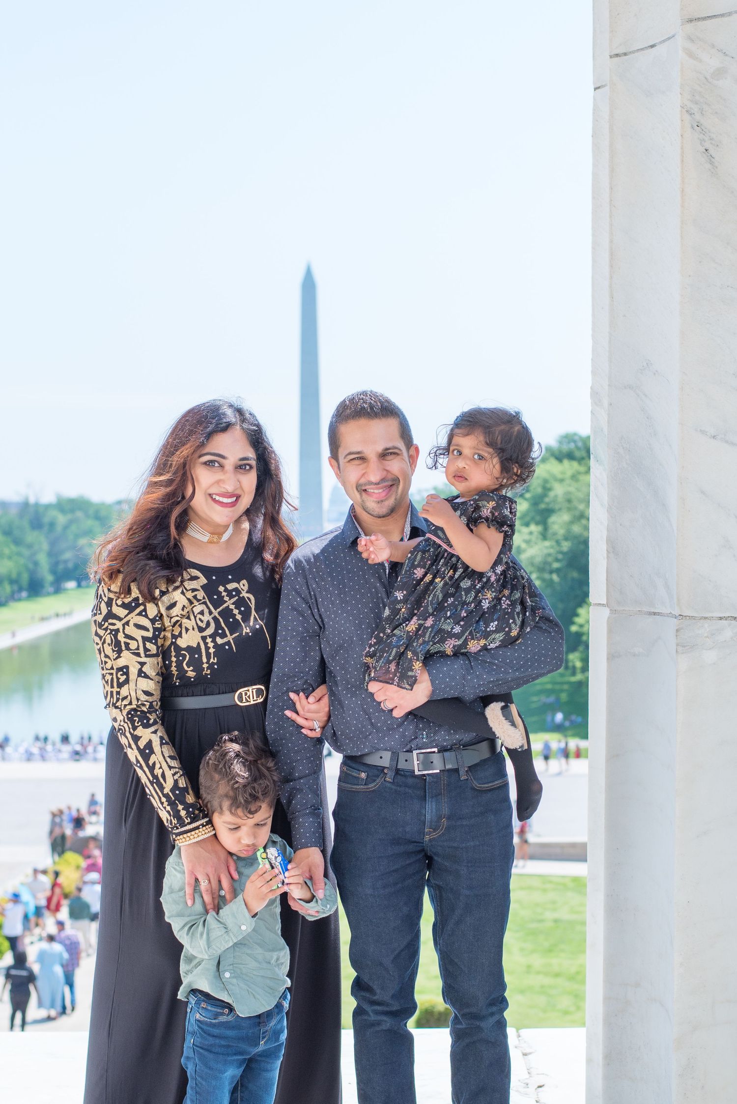 family of four look at camera with Washington Monument behind them, son holds toy car