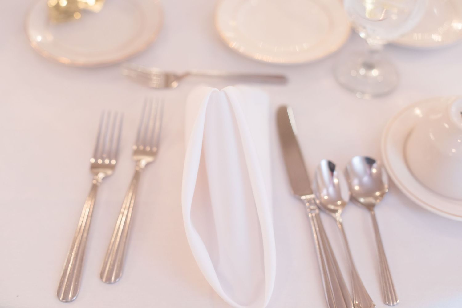 Formal place settings with white plates, silver cutlery and crystal glasses at wedding reception.