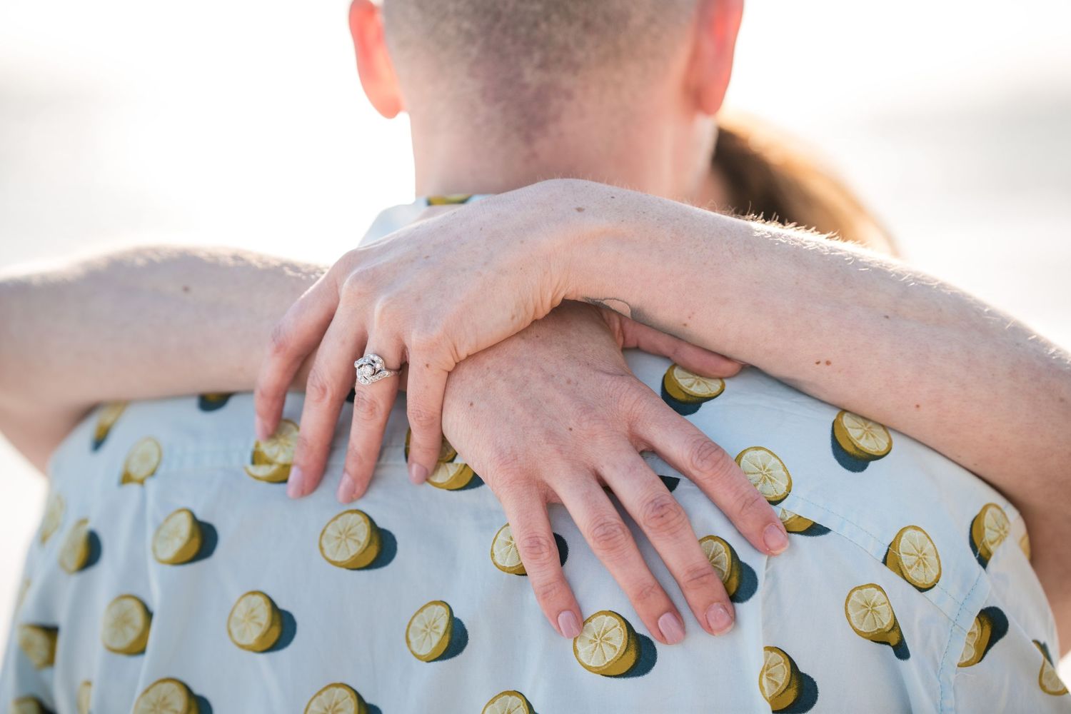 Close-up of hands resting on a shirt with avocado print pattern against bright background.