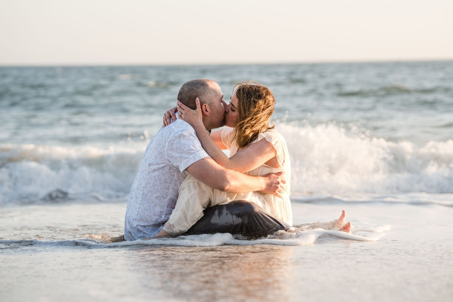 A romantic couple shares a tender moment while sitting in the surf at the beach.