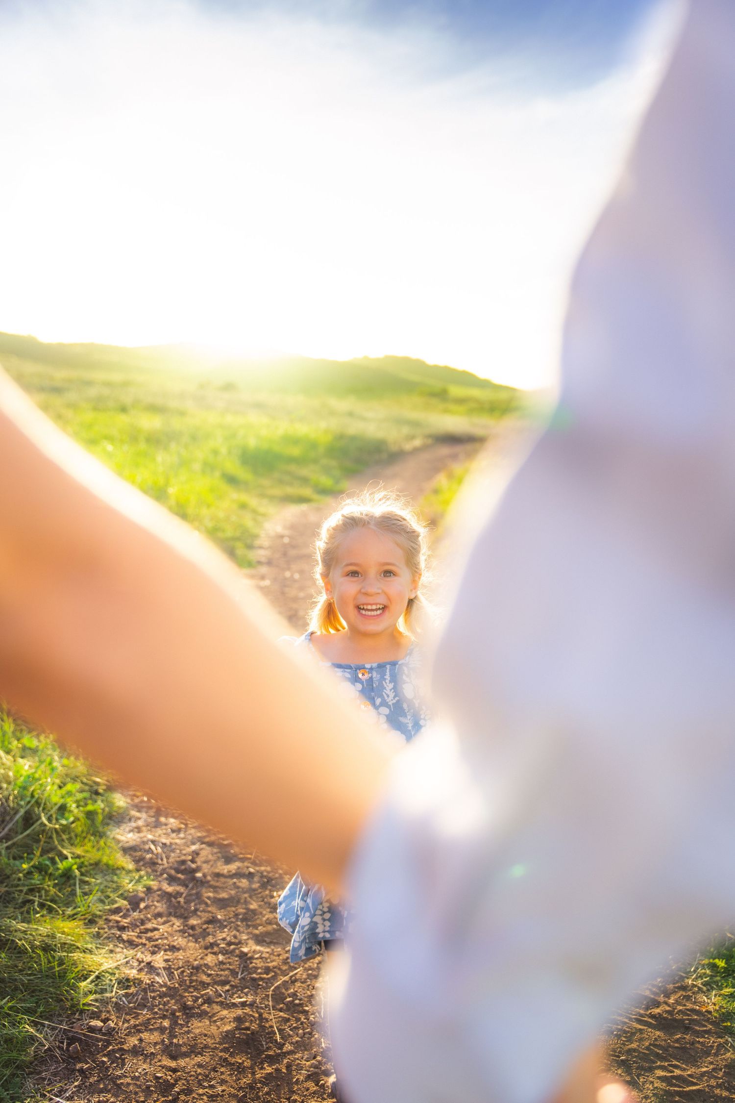 A sunlit path through green hills with blurred foreground elements framing the scene.