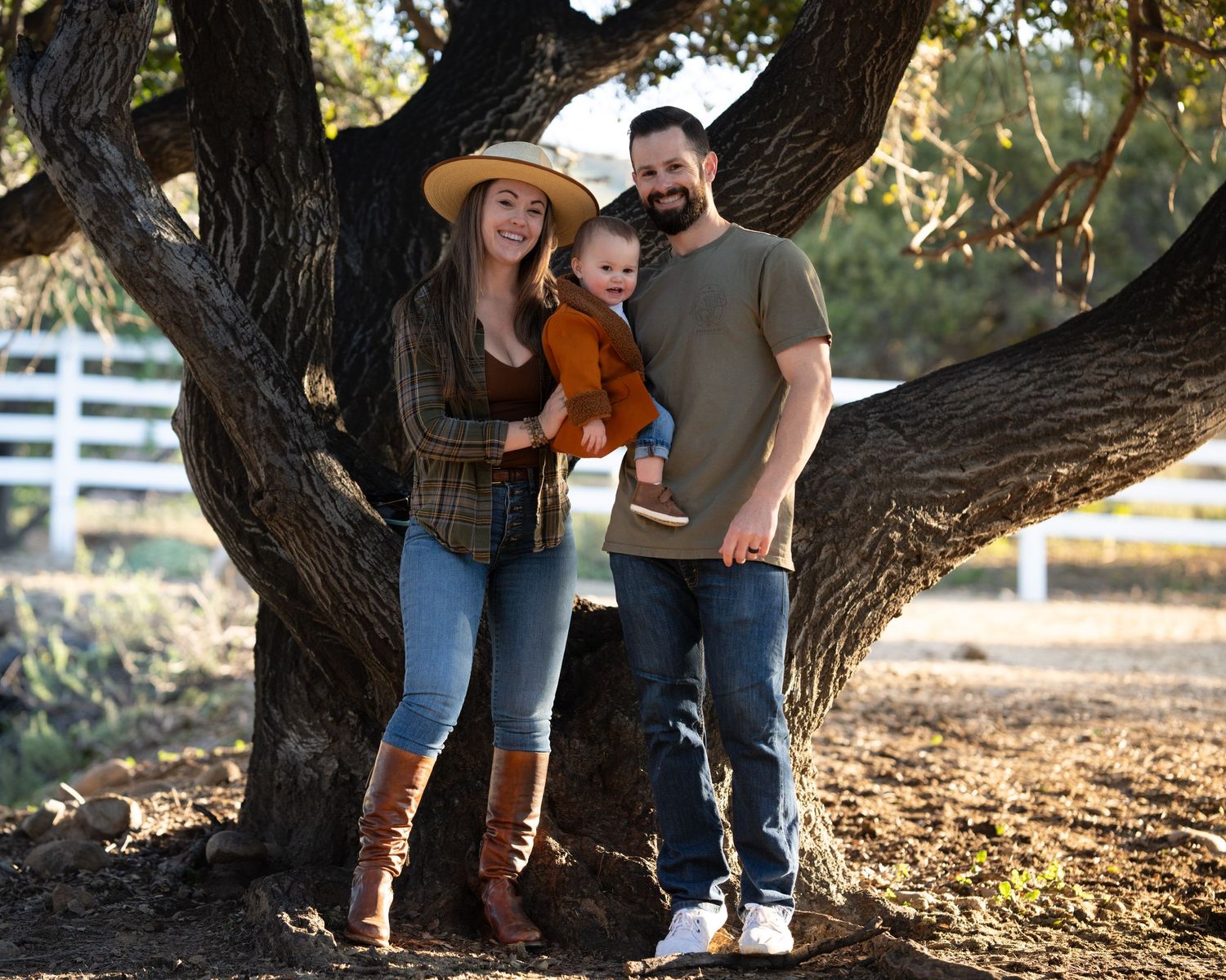 Family posing together by large tree trunk in casual fall attire.