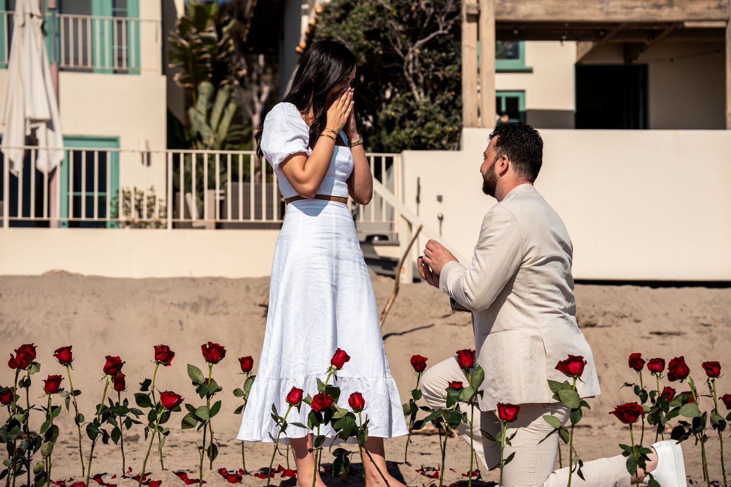 Romantic beach proposal setup with red roses and couple sharing special moment.