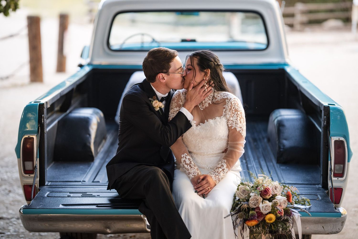 Newlyweds sharing an intimate moment in vintage pickup truck bed with bouquet.