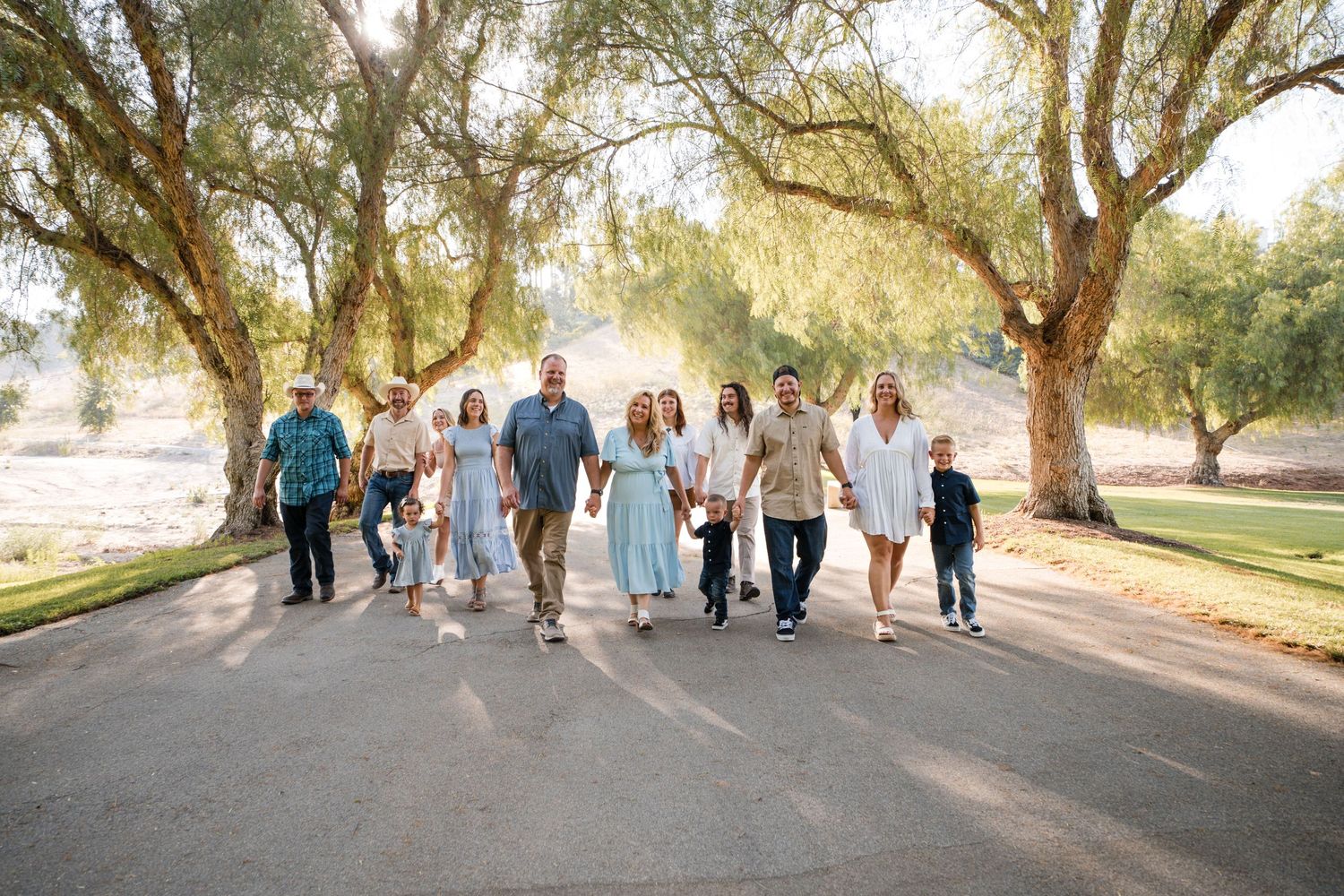 A large group walks together down a tree-lined path on a sunny day.