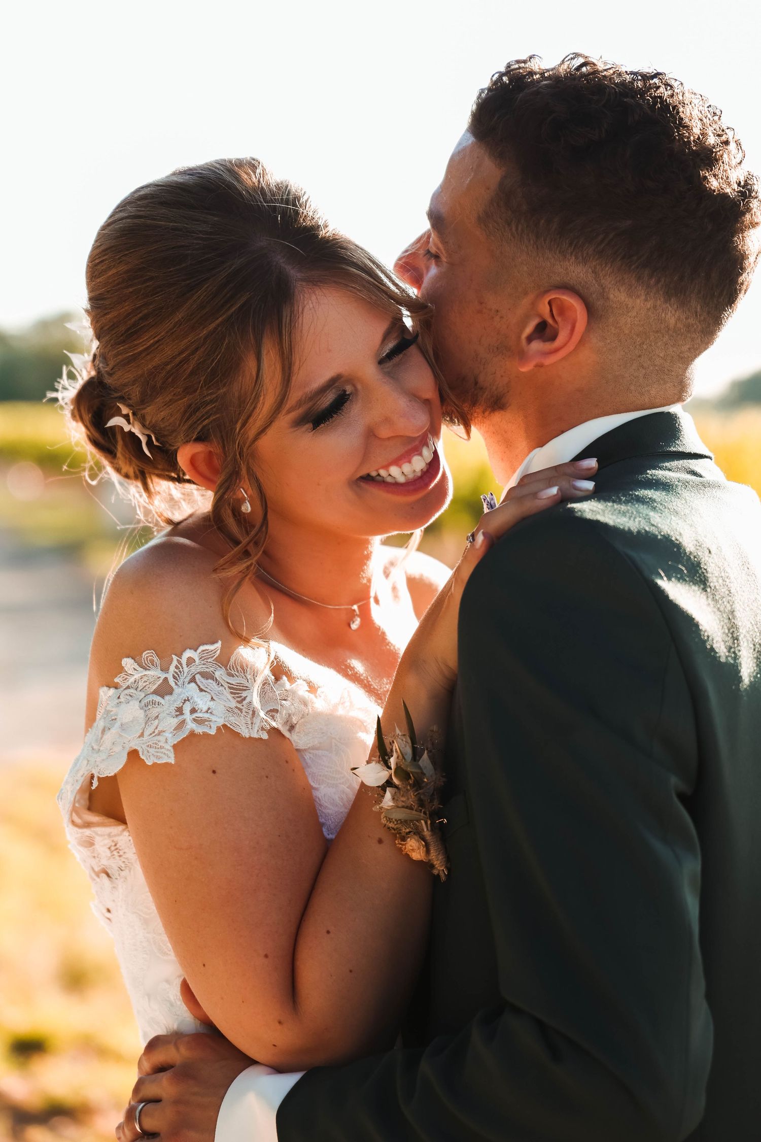 Sunlit intimate moment between couple with bride in off-shoulder lace wedding dress.