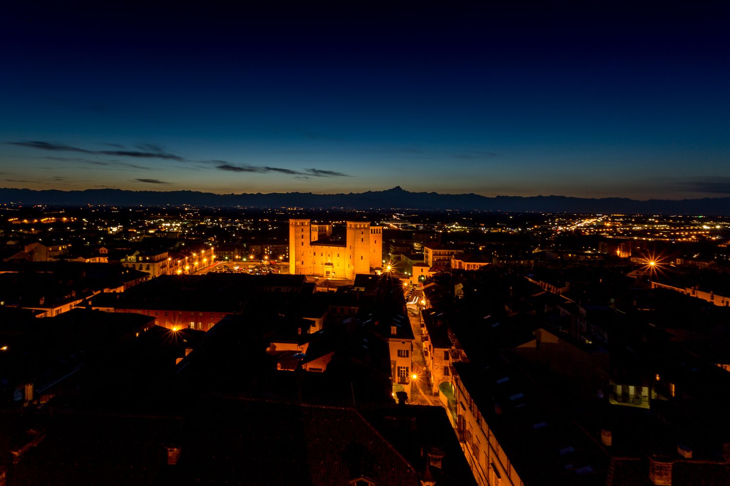 Illuminated cityscape at dusk with historic architecture and glowing streets.