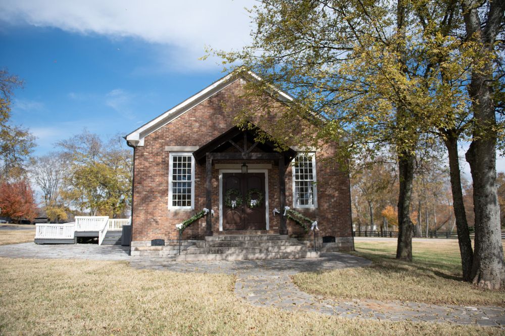 Historic brick chapel with white trim and windows surrounded by autumn trees.