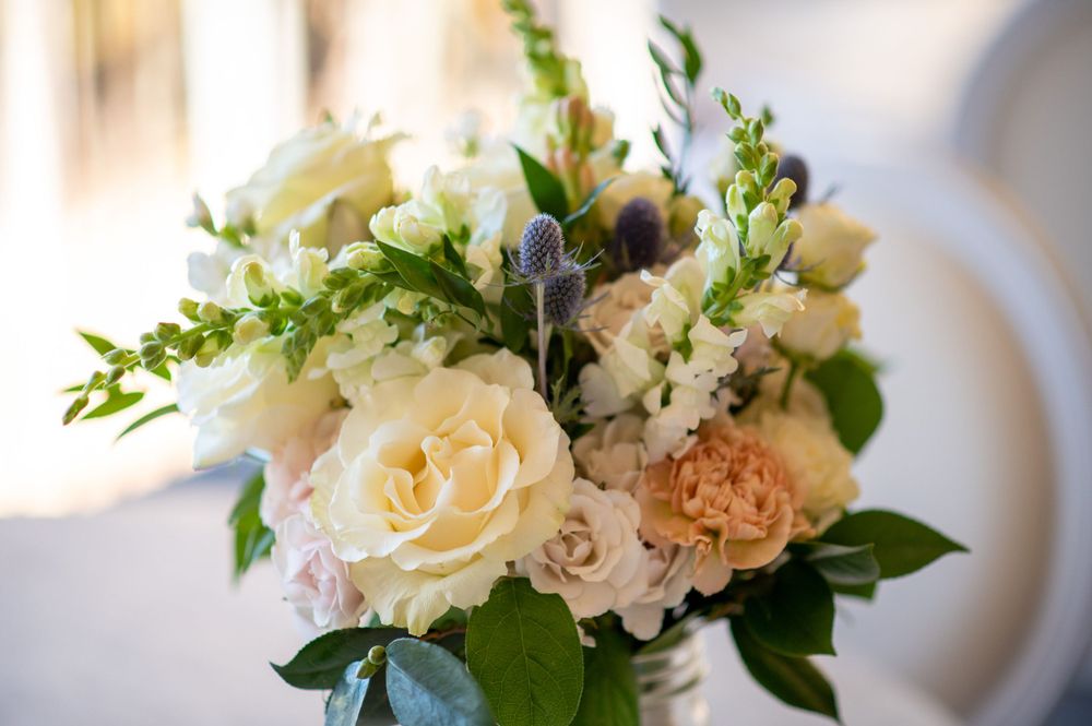 Romantic white and cream floral centerpiece with roses and greenery for a wedding reception.