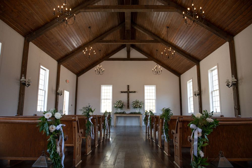 Chapel interior with wooden beams, chandeliers and pews decorated with greenery for a wedding ceremony.