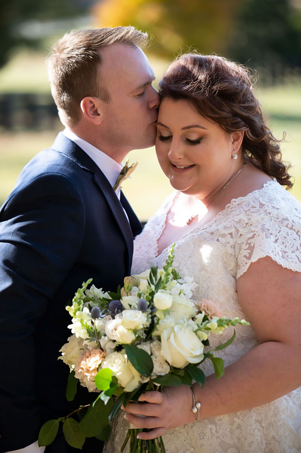 Tender wedding moment captured outdoors with a beautiful bouquet of white roses.