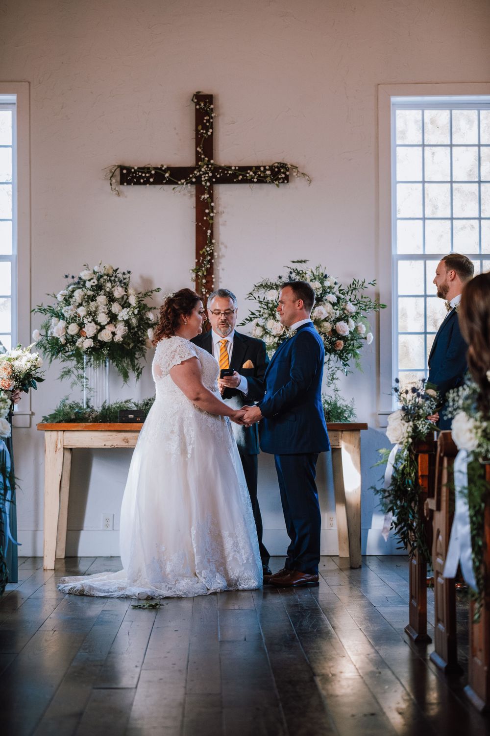 Wedding ceremony sequence in a minimalist white chapel with floral arrangements and wooden cross.