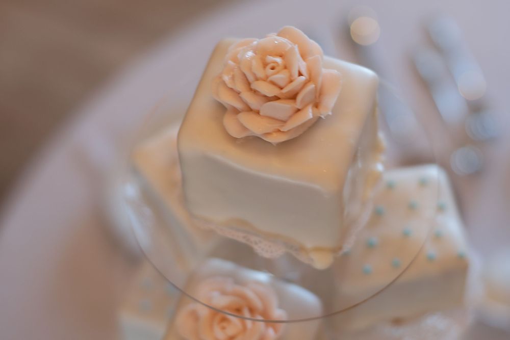 Elegant white wedding cake square with delicate peach sugar rose decoration.