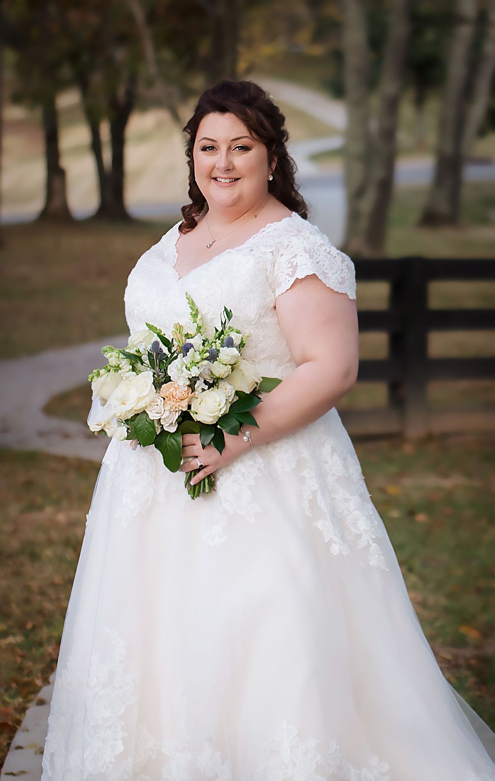 White wedding gown with delicate lace details and a bouquet of fresh flowers in outdoor setting.