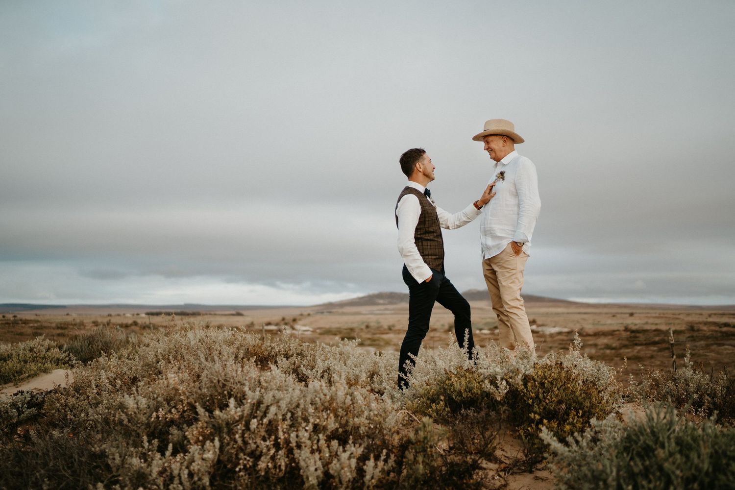 A couple stands together in rugged terrain under an overcast sky.