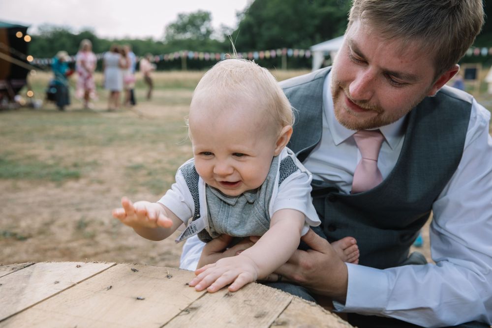 A heartwarming moment between father and baby on a wooden table at an outdoor wedding.