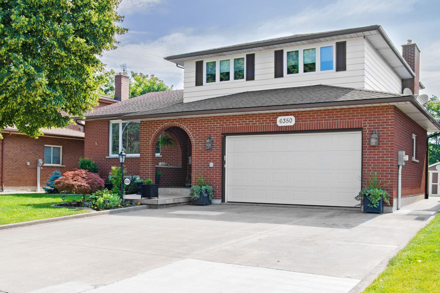 Modern brick house with white garage door and arched entryway surrounded by landscaping.