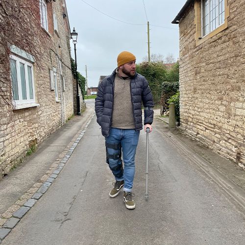 A person walking with crutches down a narrow stone-walled village street.