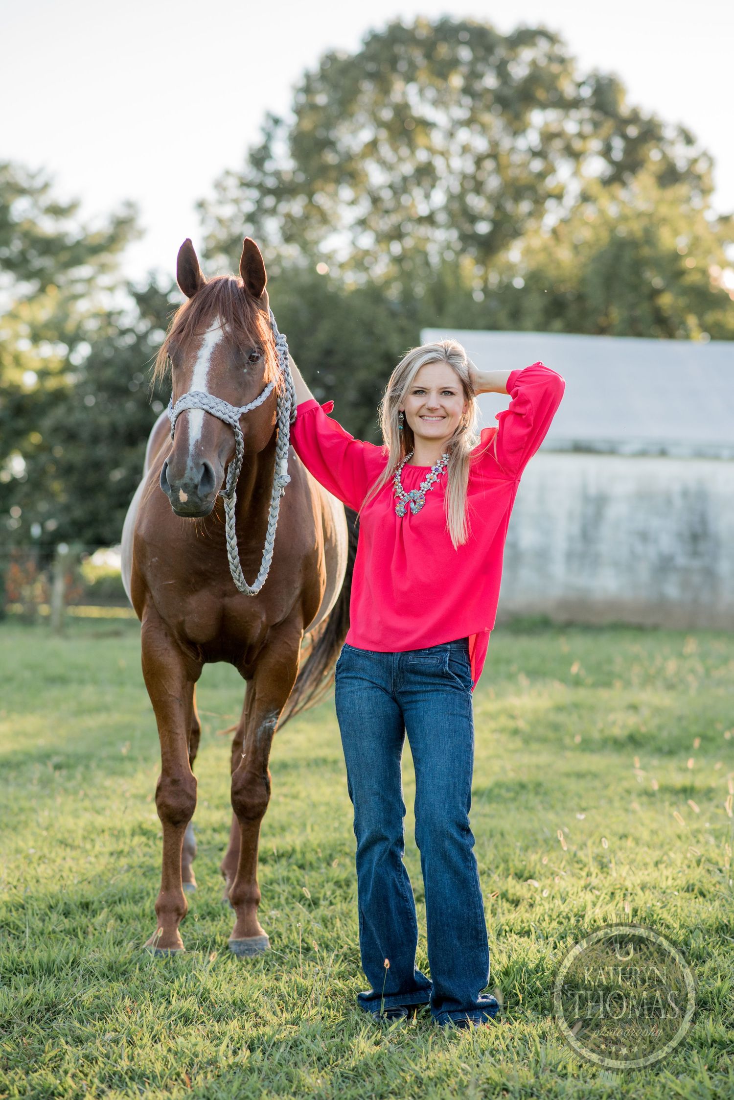 A well-groomed brown horse poses with its companion wearing a vibrant red sweater in a grassy field.