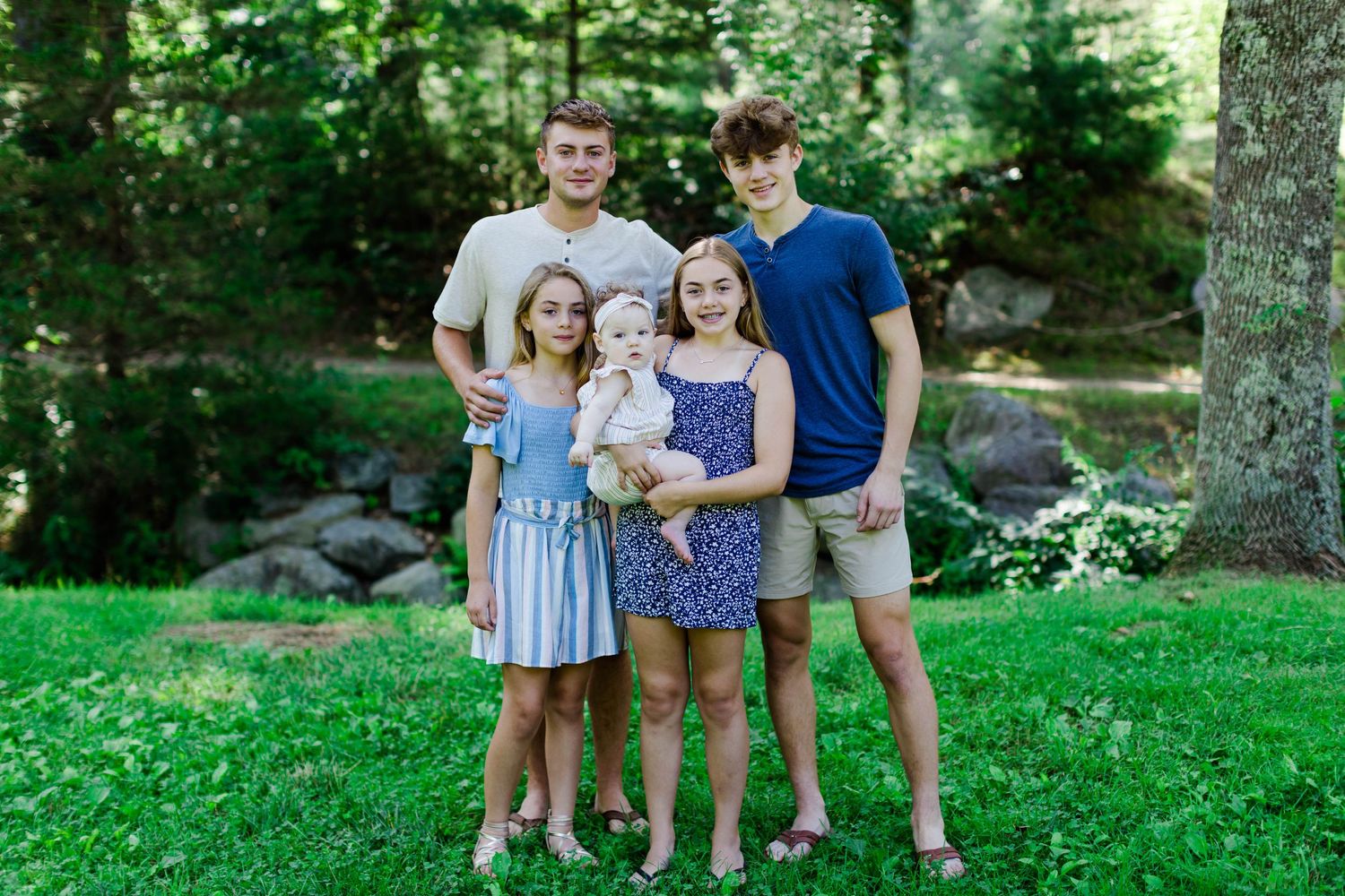 Summer portrait session in a lush garden setting with people wearing coordinating blue and white outfits.